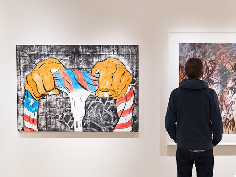 A person views a vibrant painting of hands twisting a striped, red, white, and blue cloth. The tone is thought-provoking and expressive.