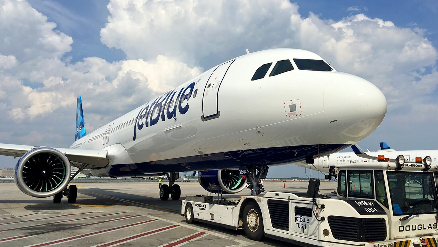 A large white airplane is parked on the tarmac, ready for its next flight under a clear blue sky.