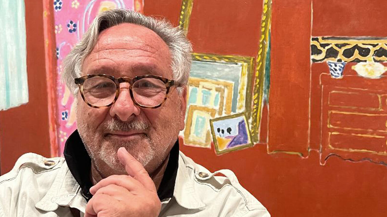 A man with glasses stands in a white shirt, smiling while posing for a photograph.