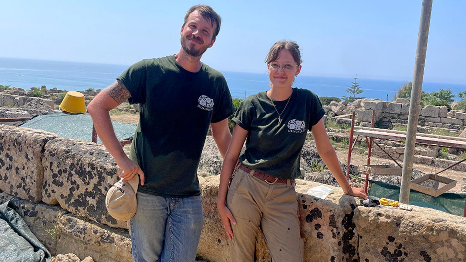 Two individuals in green shirts stand on a stone wall, smiling and enjoying their surroundings.