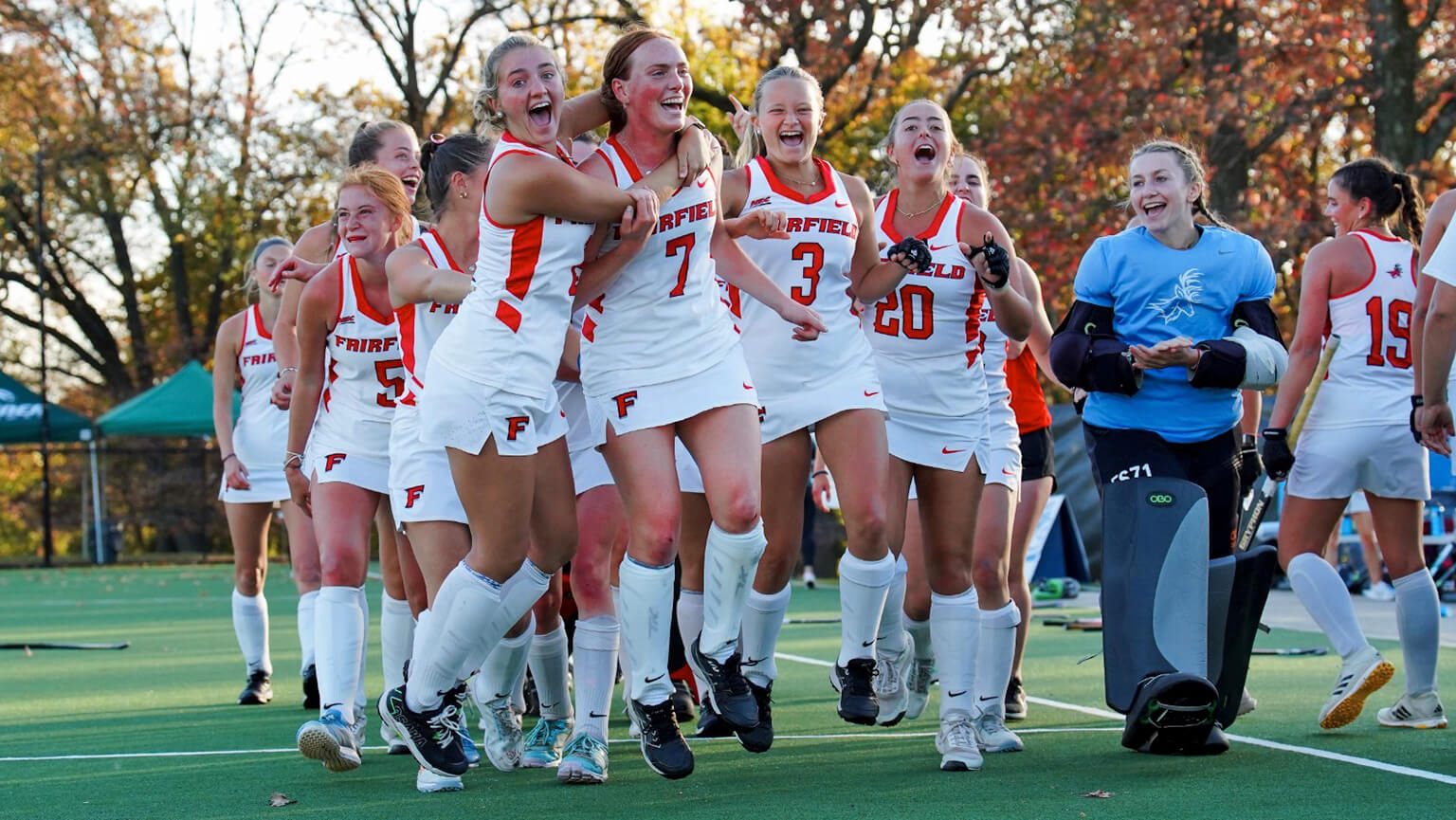 Members of a women's field hockey team cheer and embrace after successfully scoring a goal during a match.