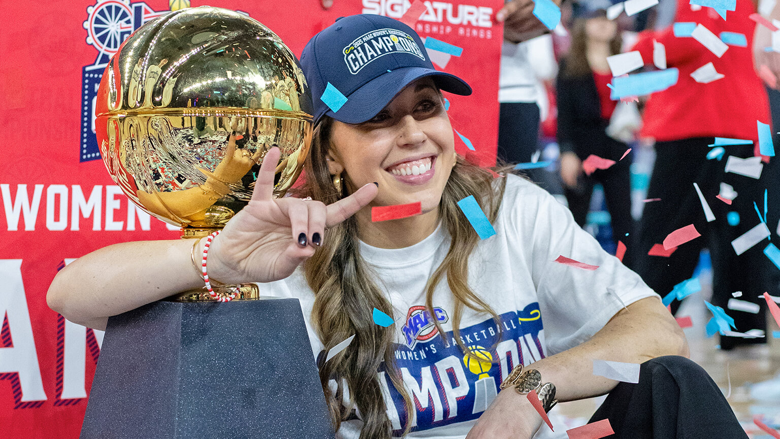 A woman beams while holding a trophy, with vibrant confetti cascading around her in a festive atmosphere.