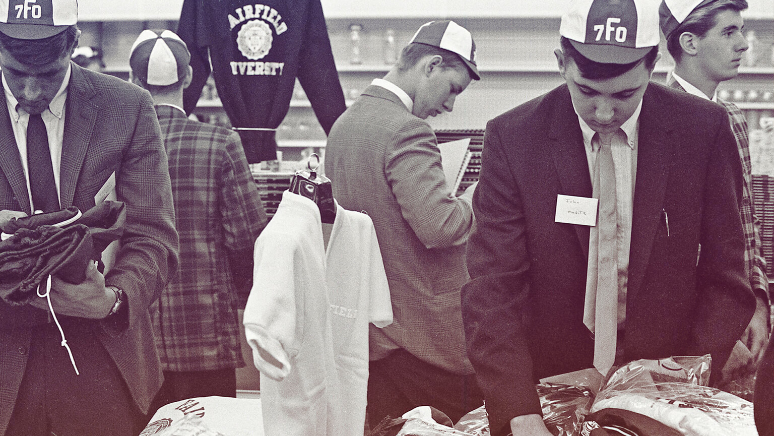 A group of students in suits and ties gathered around a table, engaged in discussion and shopping.  