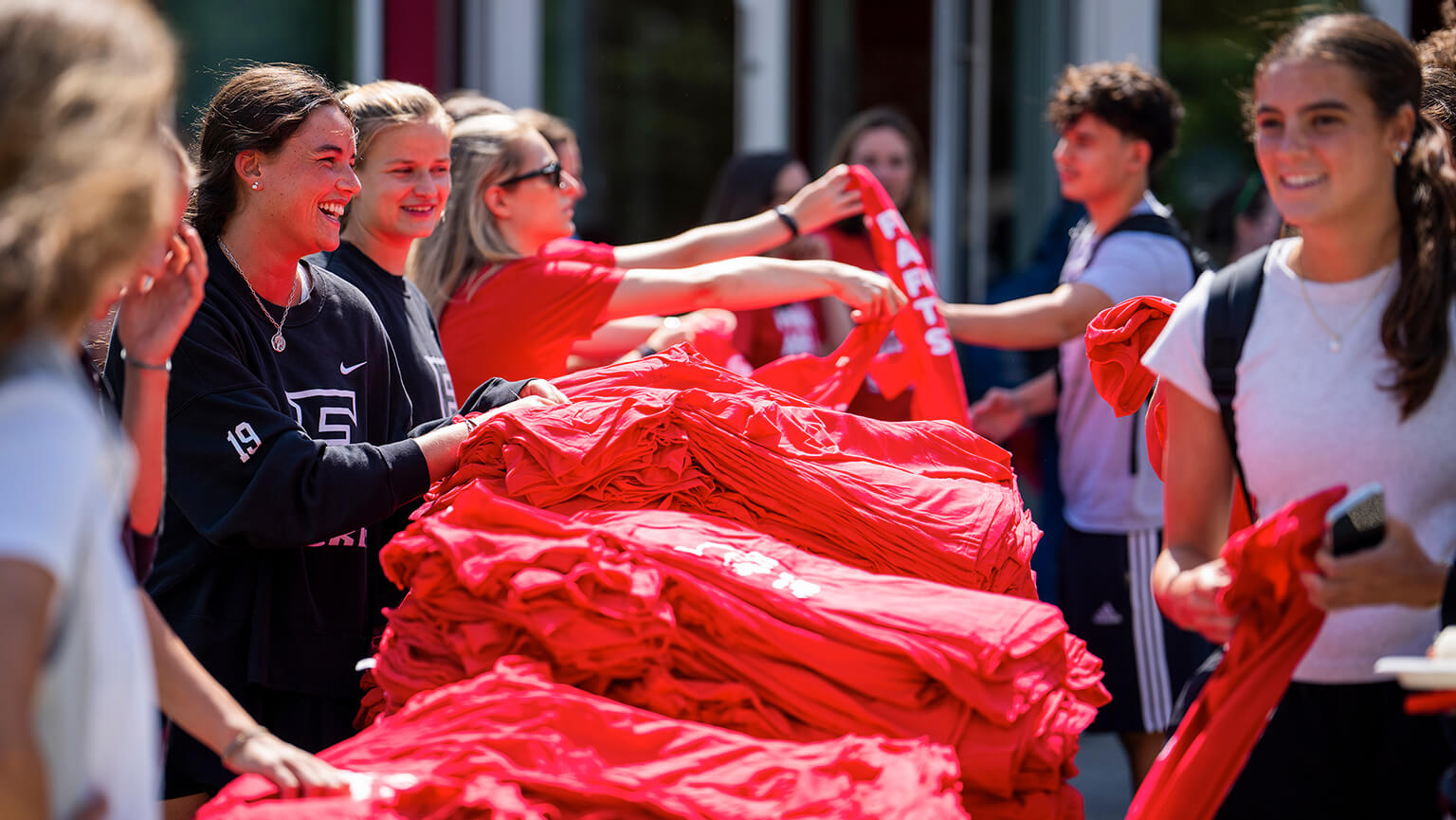 Several students stand around a table, organizing and handing out red Fairfield shirts.