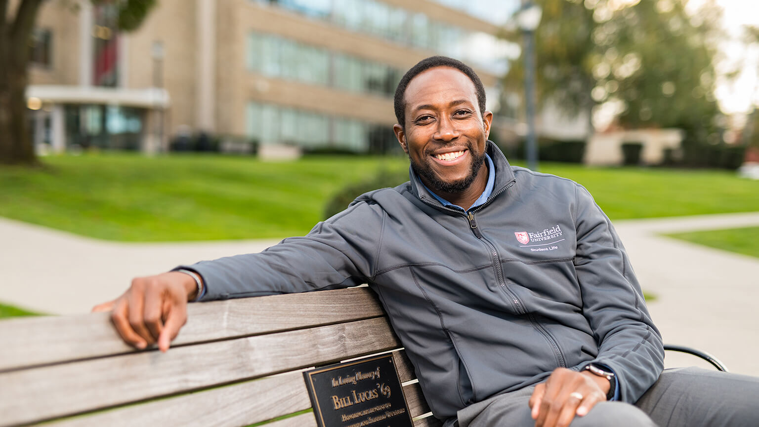 Will Johnson, PhD sitting on a bench in front of a building, casually observing his surroundings. 