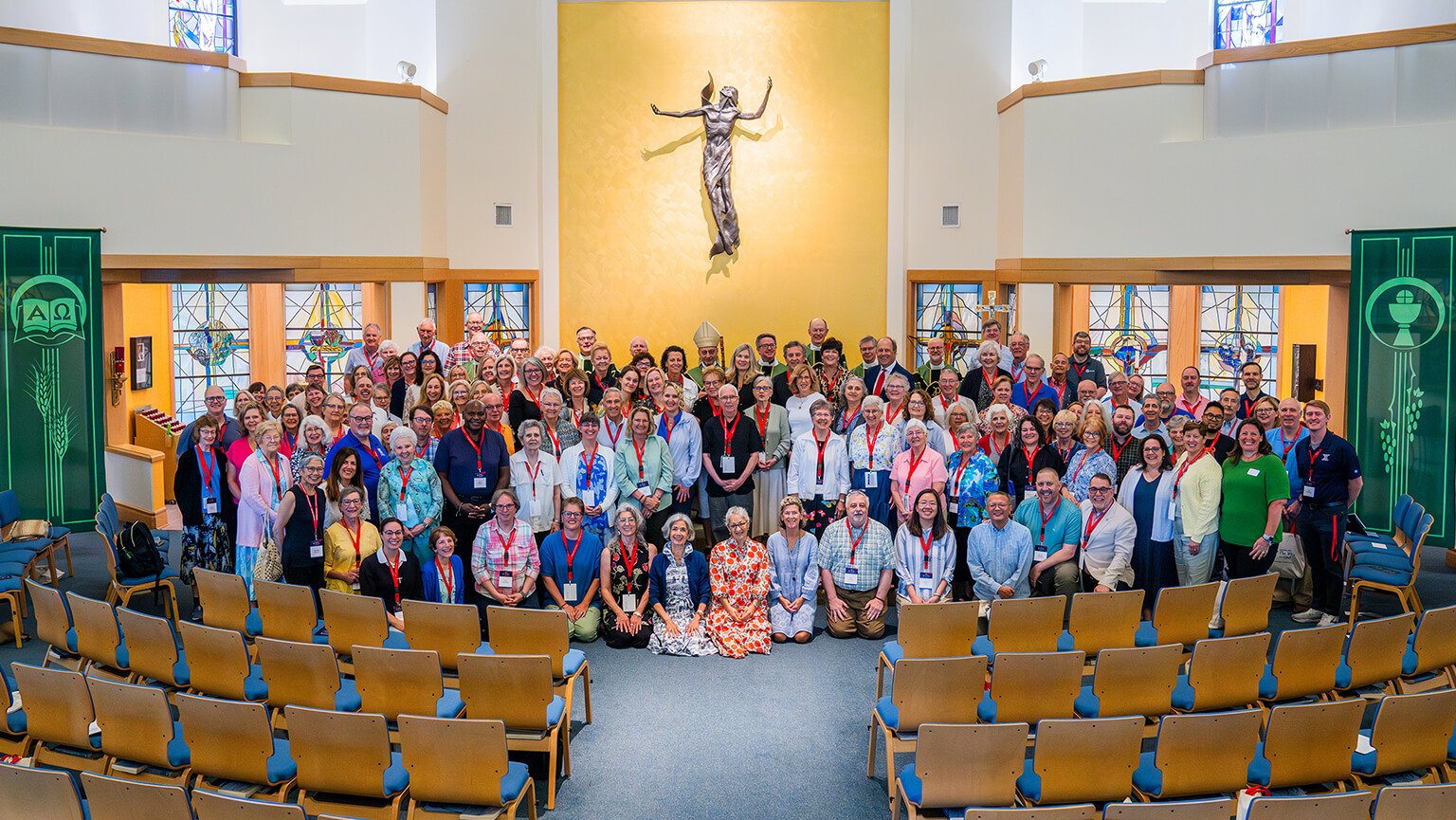 A diverse congregation poses in a church beneath a central crucifix, framed by stained-glass windows and blue pews; the scene feels warm and welcoming.