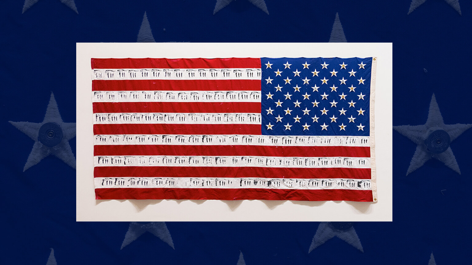 The image shows a U.S. flag with alternating red and white stripes; the white stripes feature small, black stitched figures. The blue field contains stars. The artwork conveys a sense of commentary or questioning, merging traditional patriotism with subtle messages.