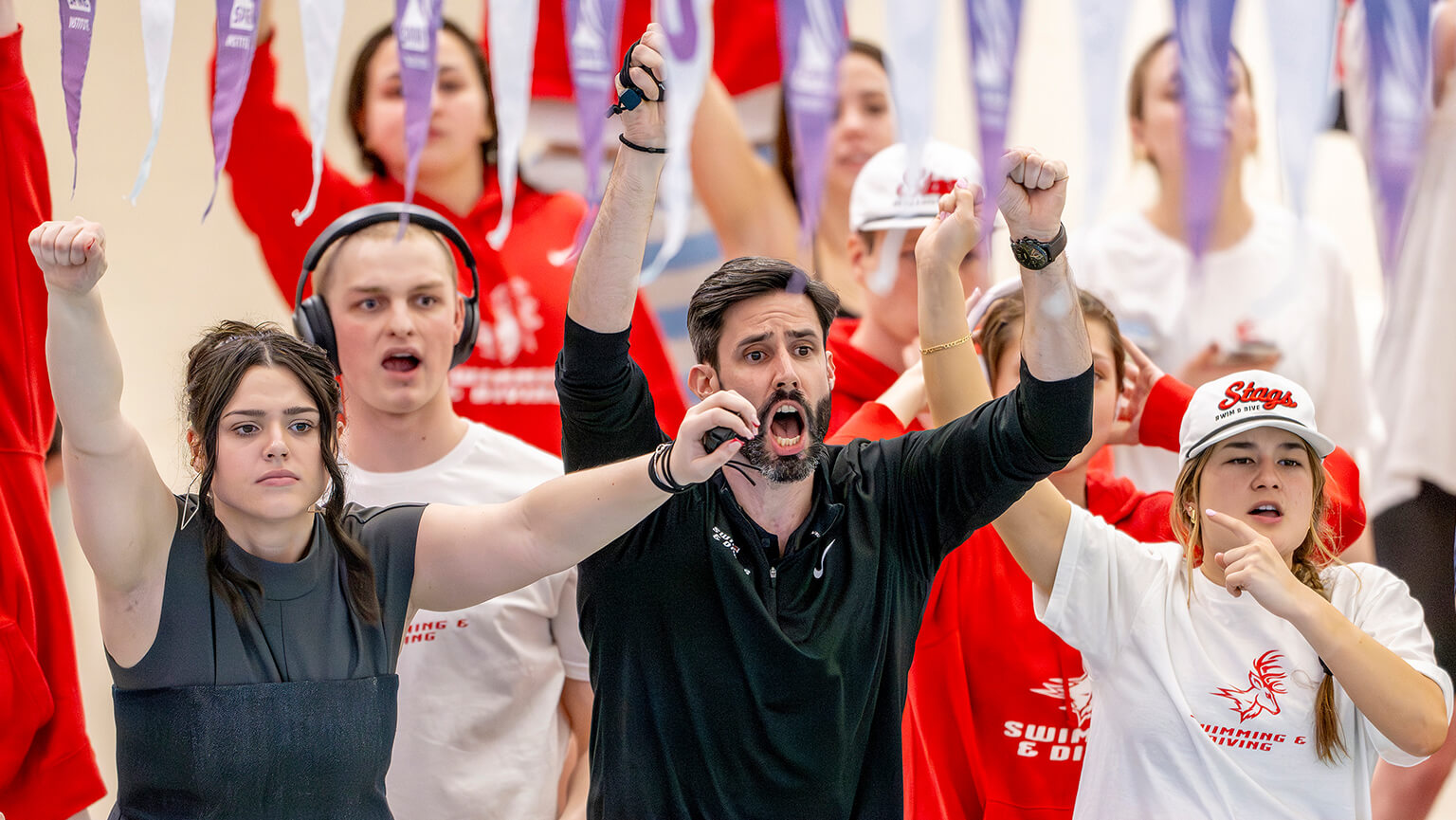 A group of people in red and white cheering enthusiastically at a sporting event. The mood is energetic and supportive, with raised fists and excited expressions.