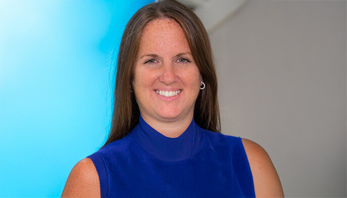 A smiling woman in a blue shirt poses for the camera, radiating positivity and warmth.