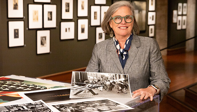 A woman with glasses stands next to a table filled with an assortment of pictures.