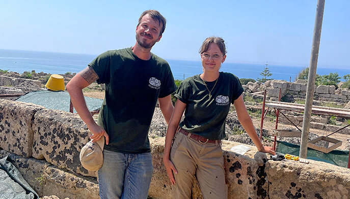 Two individuals in green shirts stand on a stone wall, smiling and enjoying their surroundings.