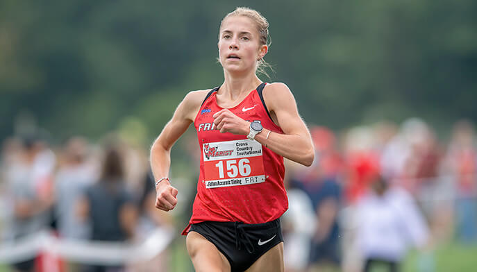 A female runner wearing a red shirt, captured mid-stride on a running path. 