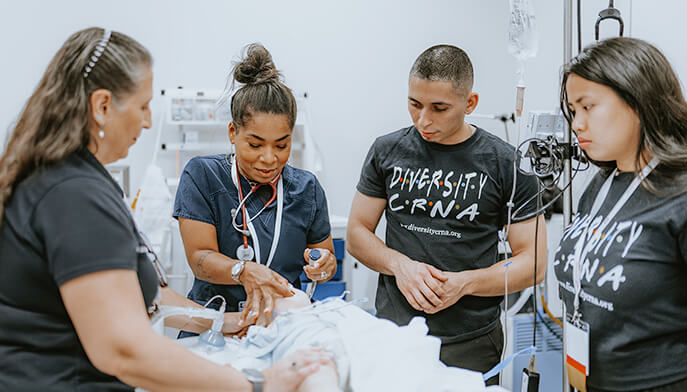 A group of diverse individuals gathered in a hospital classroom setting, engaged in conversation and supporting a patient. 