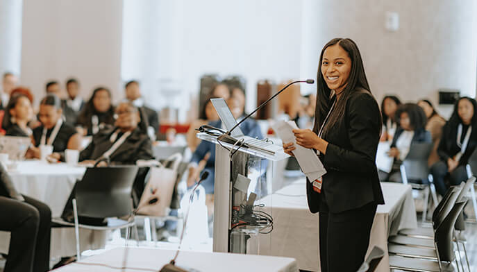 A woman in a business suit stands at a podium, confidently delivering a speech to an audience. 
