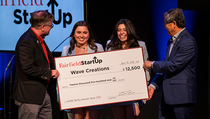 Four people stand together, holding a large check that signifies their victory in a startup competition, with joyful expressions.