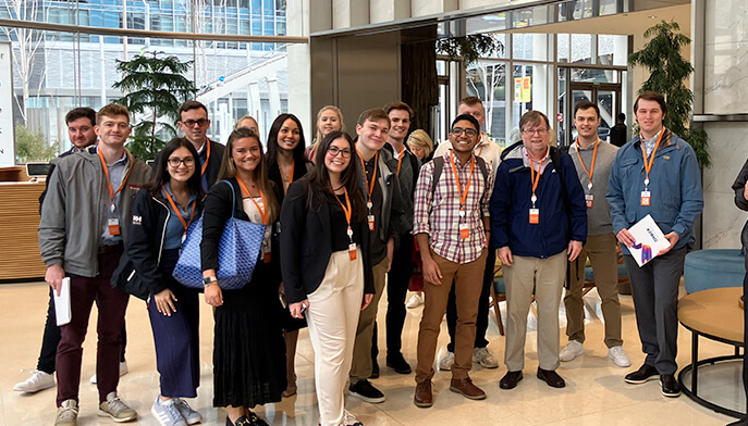 A cheerful group of students standing together for a photo in a spacious lobby area in a business building.