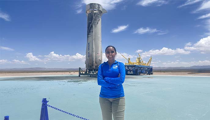 Image of Manjot Singh ’23 wearing a blue shirt stands confidently in front of a towering structure