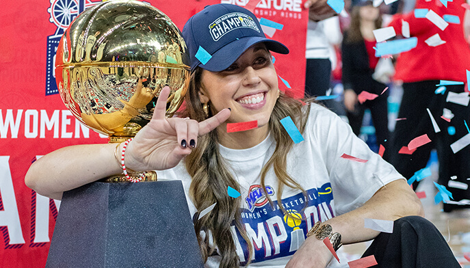 A woman beams while holding a trophy, with vibrant confetti cascading around her in a festive atmosphere.