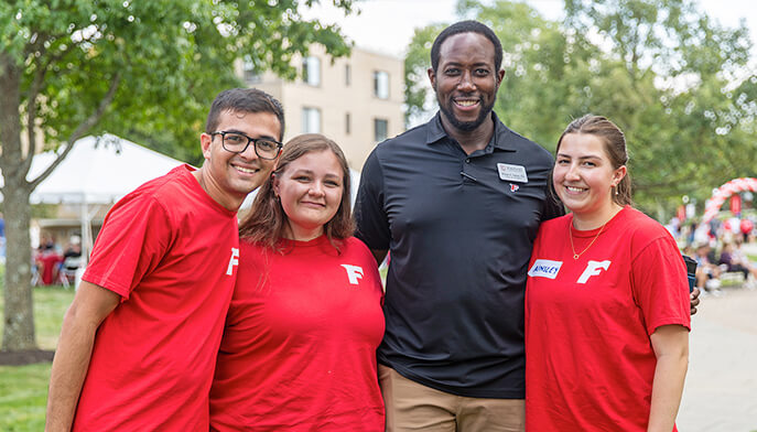 A group of four people, some wearing red shirts, standing together and smiling for a picture.