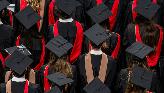 Overhead view of graduates in black caps and gowns with red accents, gathered closely at a graduation ceremony in a celebratory mood.
