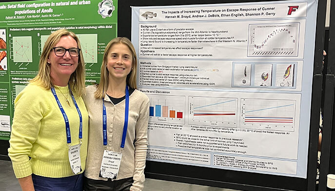 Two people smiling in front of a scientific poster presentation. The poster includes graphs and text about the effects of temperature on fish behavior.
