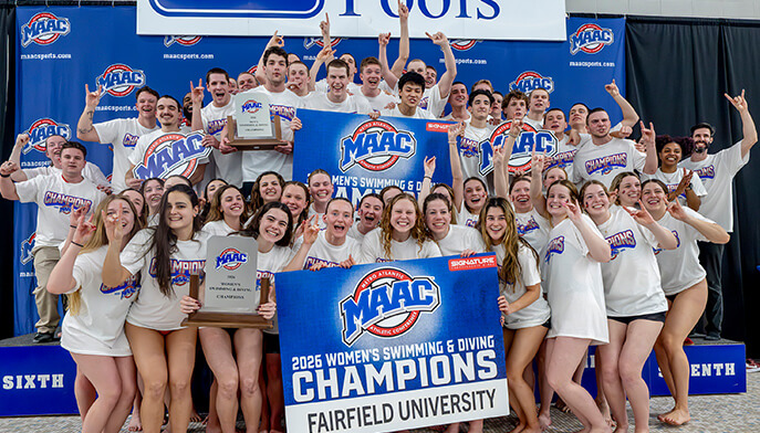 A jubilant swim team poses with trophies and a banner reading 2026 Women's Swimming & Diving Champions, Fairfield University. Smiles and raised hands convey celebration.