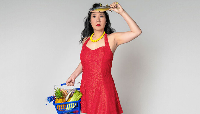 A woman stands smiling, holding a basket filled with various groceries.