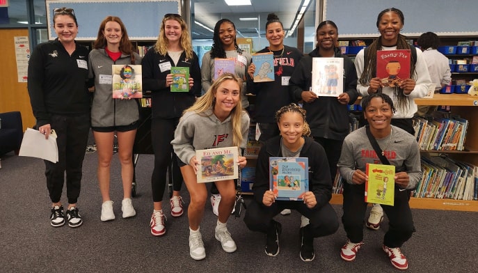 Public grade school kids posing with a Fairfield staff member while holding books in a library.