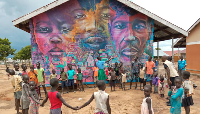 A group of children poses in front of a colorful mural on a building, featuring lively patterns and artistic elements.