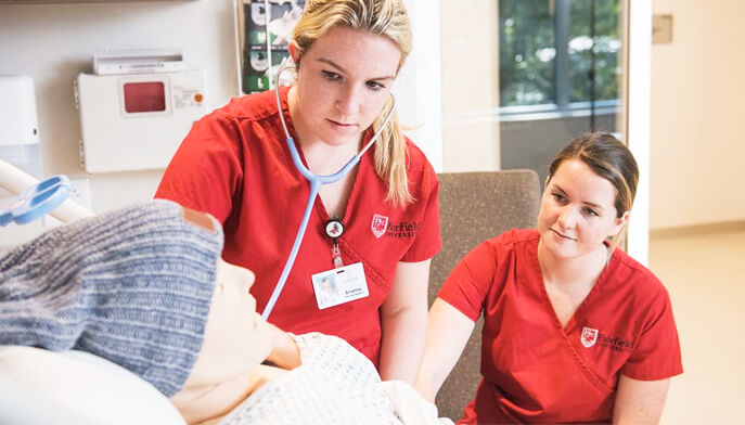 Two students practice medical procedures on a mannequin in a clinical setting, demonstrating teamwork and training techniques.