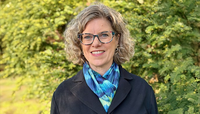 Headshot of Heidi Schlumpf as she smiles and stands against a hedge backdrop on a sunny day.