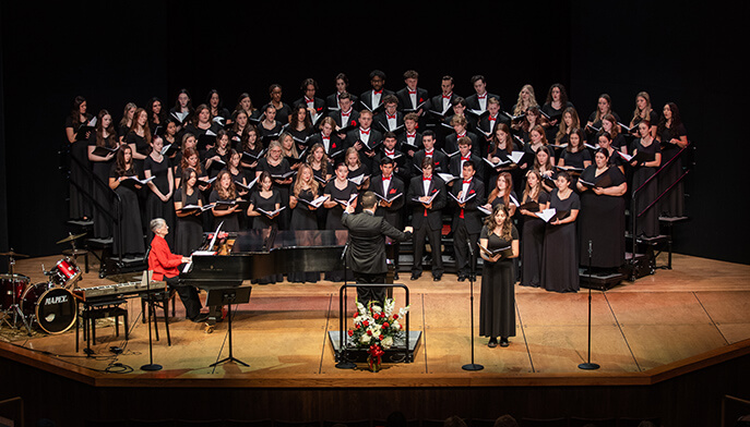 A conductor leads a choir and orchestra on stage, showcasing a collaborative musical performance.