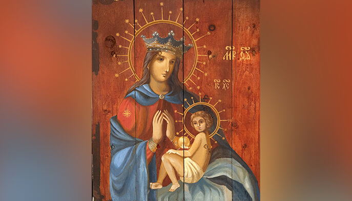 Painting of a crowned woman in a blue robe, hands clasped in prayer, holding a child on her lap. Both have halos. Background is wooden planks.