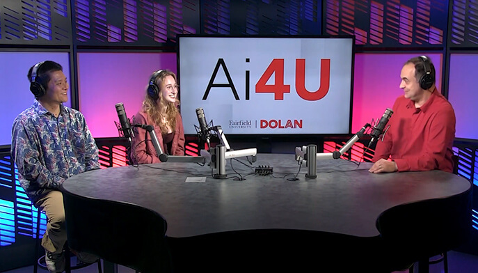 Jie Tao, DSc and two other people are seated at a podcast table with microphones, smiling and engaged in conversation. A screen behind them displays "Ai4U." The setting is modern and colorful, conveying a lively and professional atmosphere.