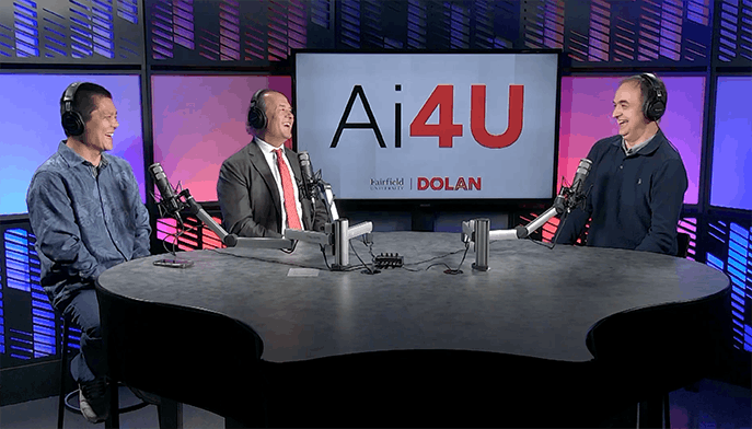 Jie Tao, DSc and two other people are seated at a podcast table with microphones, smiling and engaged in conversation. A screen behind them displays "Ai4U." The setting is modern and colorful, conveying a lively and professional atmosphere.