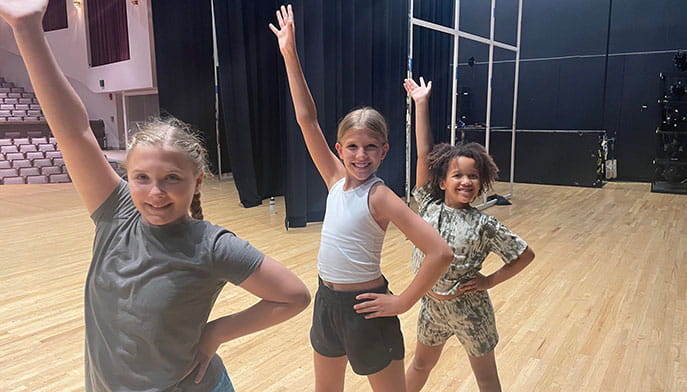 Three kids dance on the Quick Center stage with their hand in the air and smiling.