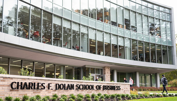 Modern glass building with the sign "Charles F. Dolan School of Business" in front. Students walk along the path, conveying an academic atmosphere.
