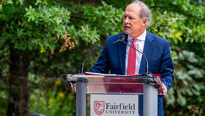 University President Mark R. Nemec, PhD giving a speech outdoors at a Fairfield-branded podium.