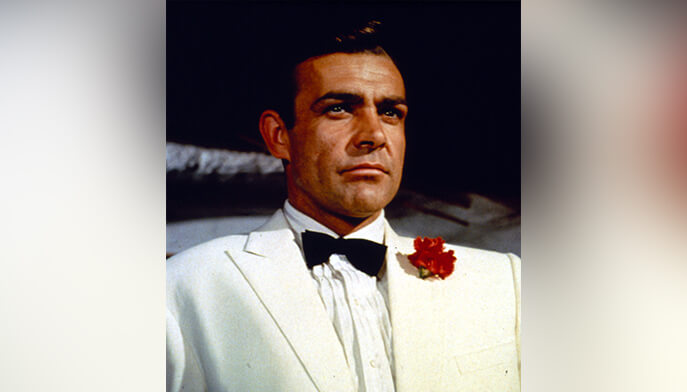 Sean Connery as James Bond in a white tuxedo with black bow tie and red boutonnière, projecting a poised, confident, serious demeanor.