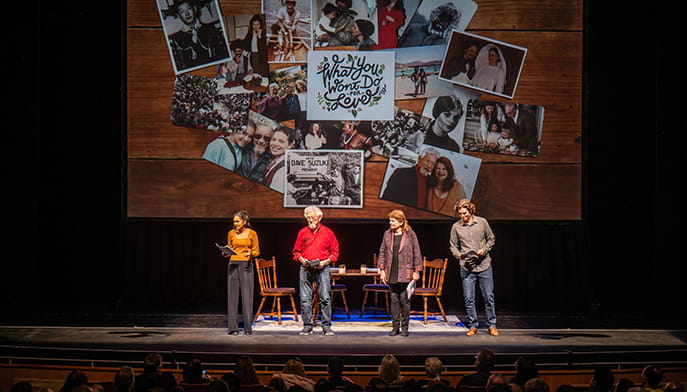 Four speakers stand on a theater stage beneath a collage of family photos and handwritten memories, addressing a seated audience in a warm, reflective setting.