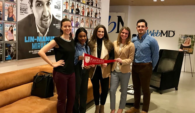 Five people standing in front of a Lin Manuel Miranda poster
