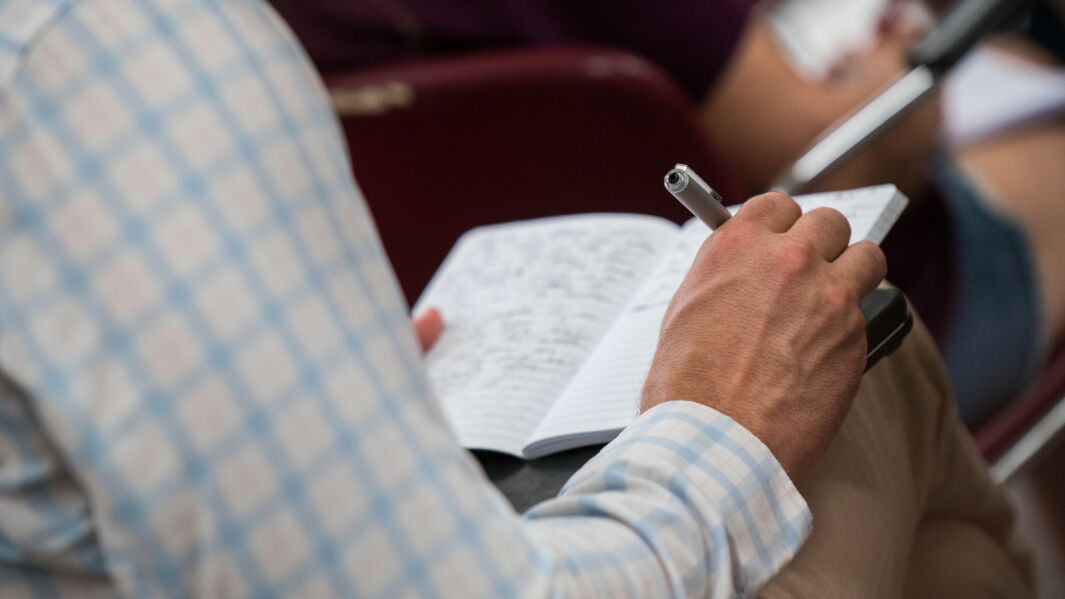 A student writes in a journal propped up on their lap.