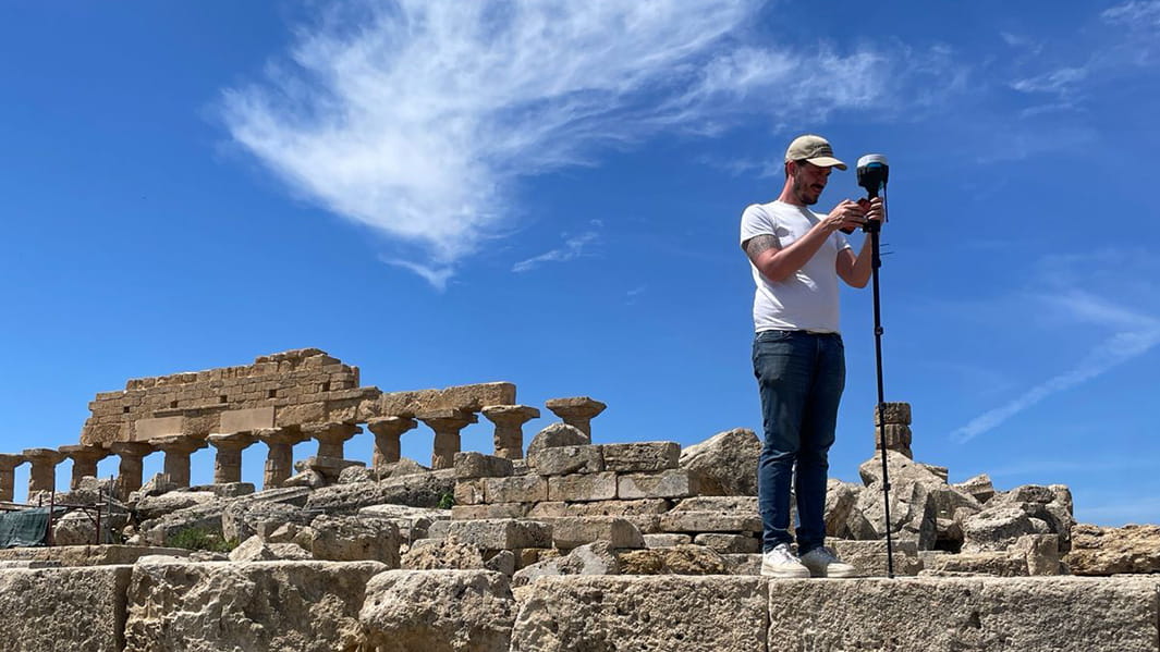 Ancient Mediterranean Studies team surveyor setting up a camera in the ruins of old architecture on a bright, sunny day.
