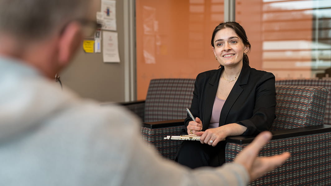 Nursing leadership candidate taking notes on a clipboard in a private office as a patient confides in her.