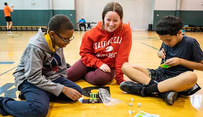 A woman and two boys are happily playing with colorful Legos on the floor, engaging in creative building activities.