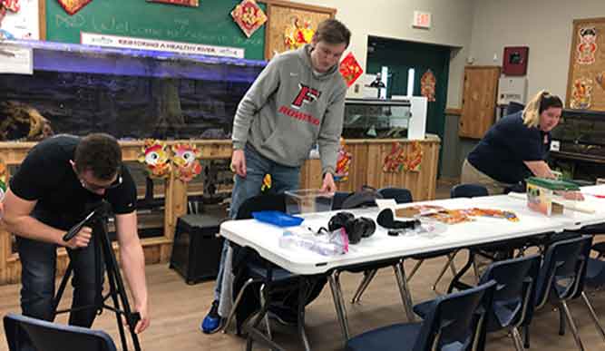 Two men collaborate on a project at a table in a classroom setting, focused and engaged in their work.