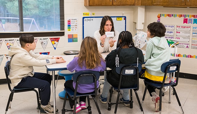 Fairfield student engaging with a small group of young, student children in a reading exercise.