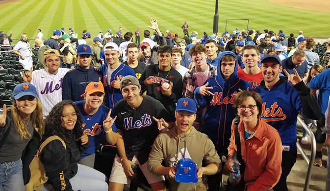A group of Fairfield University students attending a New York Mets game in a crowd with the field in the background during a night game.