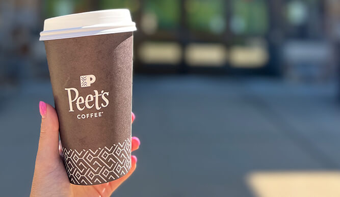 A hand grasping a coffee cup with "Peet's Coffee" printed on it.