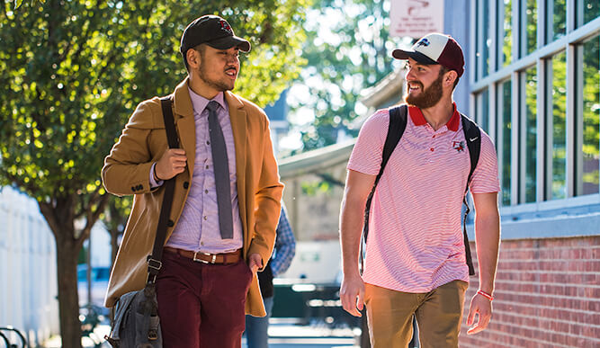 Two male students strolling down a sidewalk, appearing relaxed and friendly.